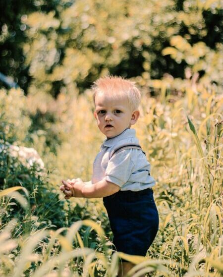 A little boy stands amidst tall grass in a sunlit summer meadow. Capturing childhood wonder.